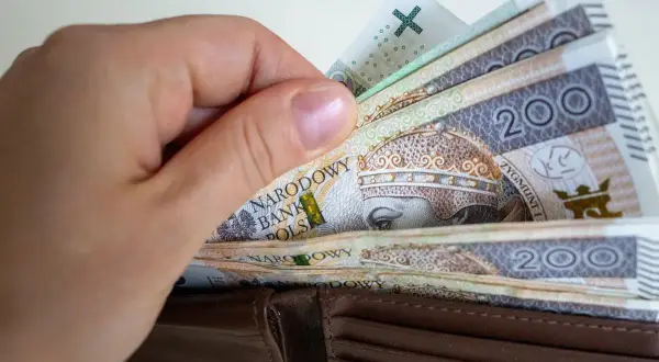 Dłoń wsuwa banknoty 200 zł do portfela. To symbol obietnic Koalicji Obywatelskiej dotyczących składki zdrowotnej dla przedsiębiorców.