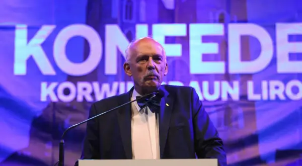 Janusz Korwin-Mikke, znany z kontrowersyjnych poglądów, przemawia na tle napisu "Konfederacja".