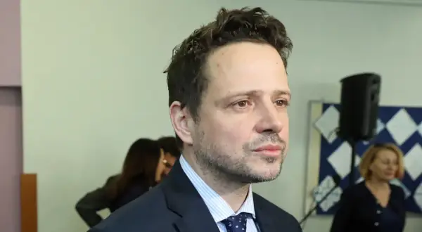 Rafał Trzaskowski, którego wykształcenie budzi zainteresowanie, w garniturze i krawacie. W tle inne osoby i tablica.