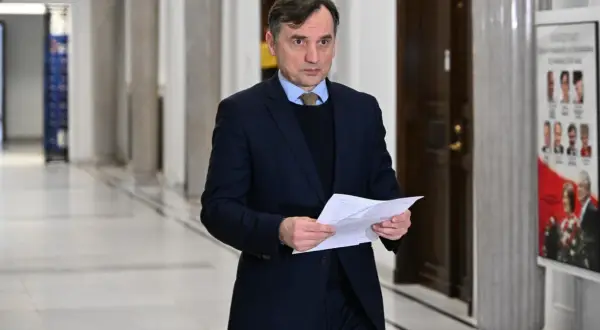 Mężczyzna w garniturze trzyma dokumenty, być może związane z aferą z Funduszem Sprawiedliwości u Ziobry i PiS.
