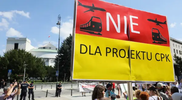 Protestujący sprzeciwiają się projektowi CPK. Transparent "NIE DLA PROJEKTU CPK" z symbolami samolotu i pociągu.