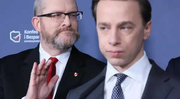 Dwóch mężczyzn w garniturach, jeden z brodą i okularami, drugi z wyrazem twarzy.