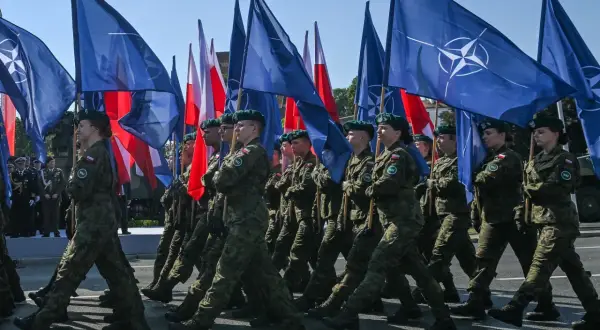 Żołnierze maszerują z flagami NATO i Polski. To obraz polityki obronnej koalicji obywatelskiej, która stawia na zakupy sprzętu wojskowego.