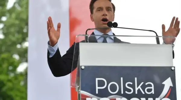 Mężczyzna przemawia przy mównicy z napisem "Polska na nowo". Konfederacja a podatki – chce znieść PIT, CIT i VAT, by uwolnić gospodarkę.