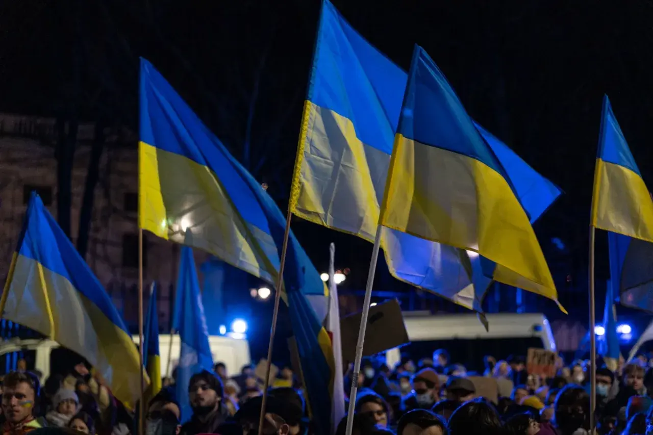 Zwolennicy pomocy militarnej dla Ukrainy i polityki obronnej kraju, z ukraińskimi flagami na nocnym wiecu.