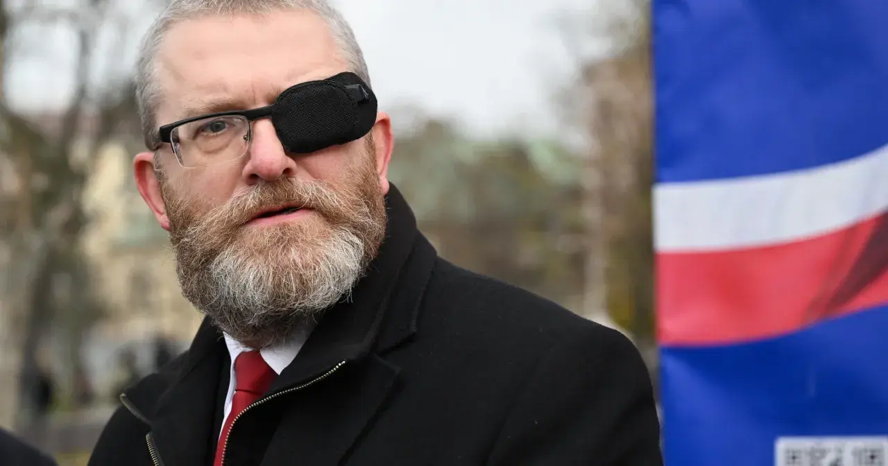 Grzegorz Braun w Sejmie, skandale i realne poparcie dla partii. Mężczyzna w okularach i opasce na oku, na tle flagi.