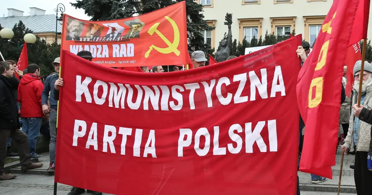 Ludzie niosą czerwony transparent "KOMUNISTYCZNA PARTIA POLSKI" i flagę z sierpem i młotem. To manifestacja poparcia dla socjalizmu.