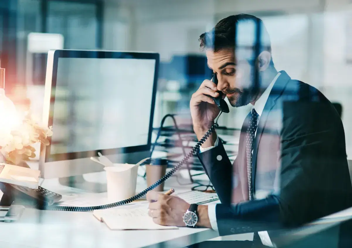 Biznesmen w garniturze rozmawia przez telefon, notując. Czasem nawet siła wyższa nie przeszkodzi w pracy.