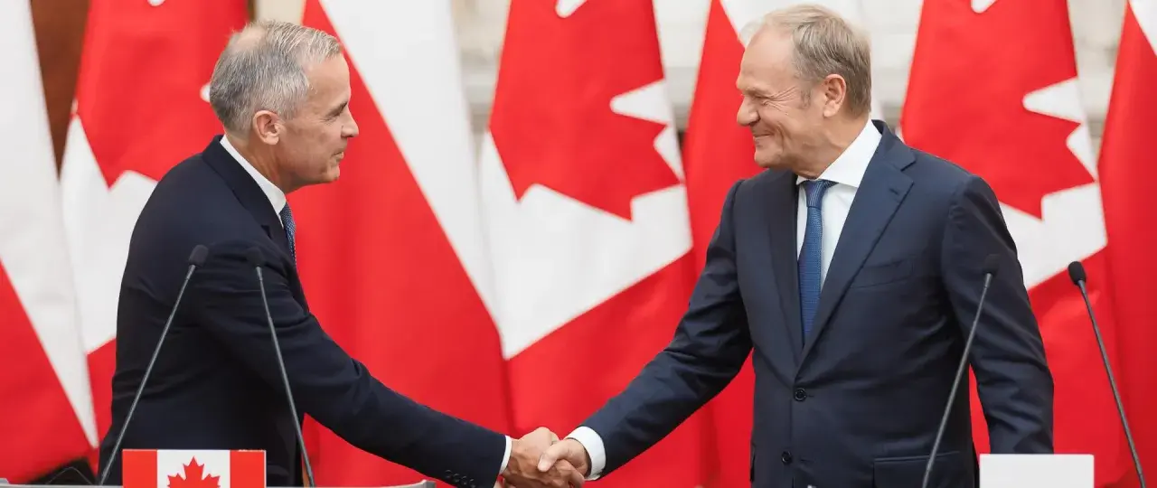 Dwóch polityków ściska sobie dłonie na tle flag Kanady. Wzmocnienie relacji polska-kanada.