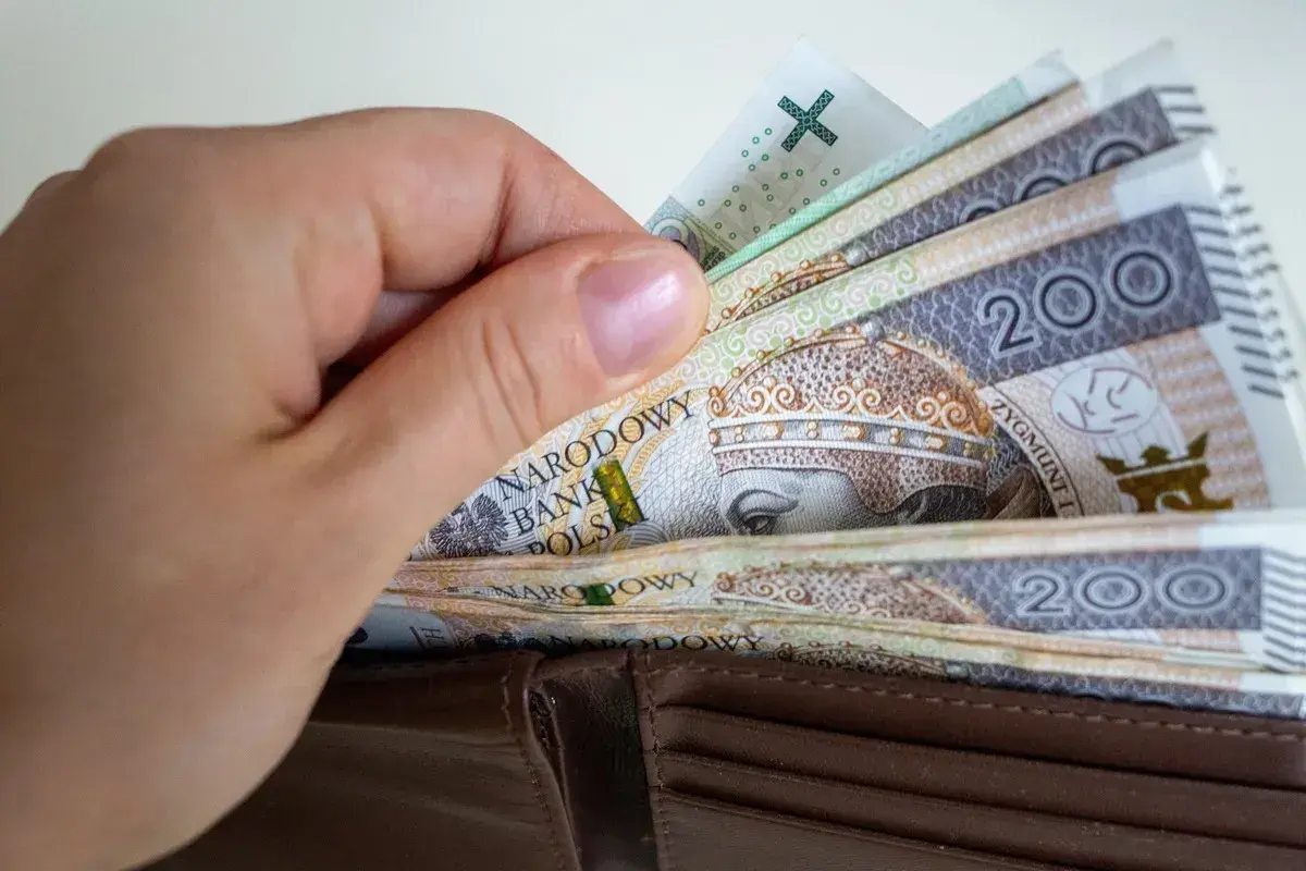 Dłoń wsuwa banknoty 200 zł do portfela. To symbol obietnic Koalicji Obywatelskiej dotyczących składki zdrowotnej dla przedsiębiorców.