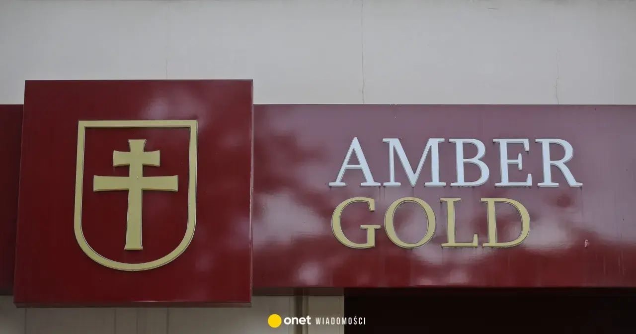 Złoty symbol krzyża na bordowym tle obok napisu AMBER GOLD.