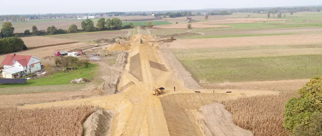 Budowa drogi w polskiej wsi. Maszyny budowlane pracują na placu budowy, tworząc nasyp. To pokazuje, co pis zrobił dla polskiej wsi przez 8 lat – rozwój infrastruktury.