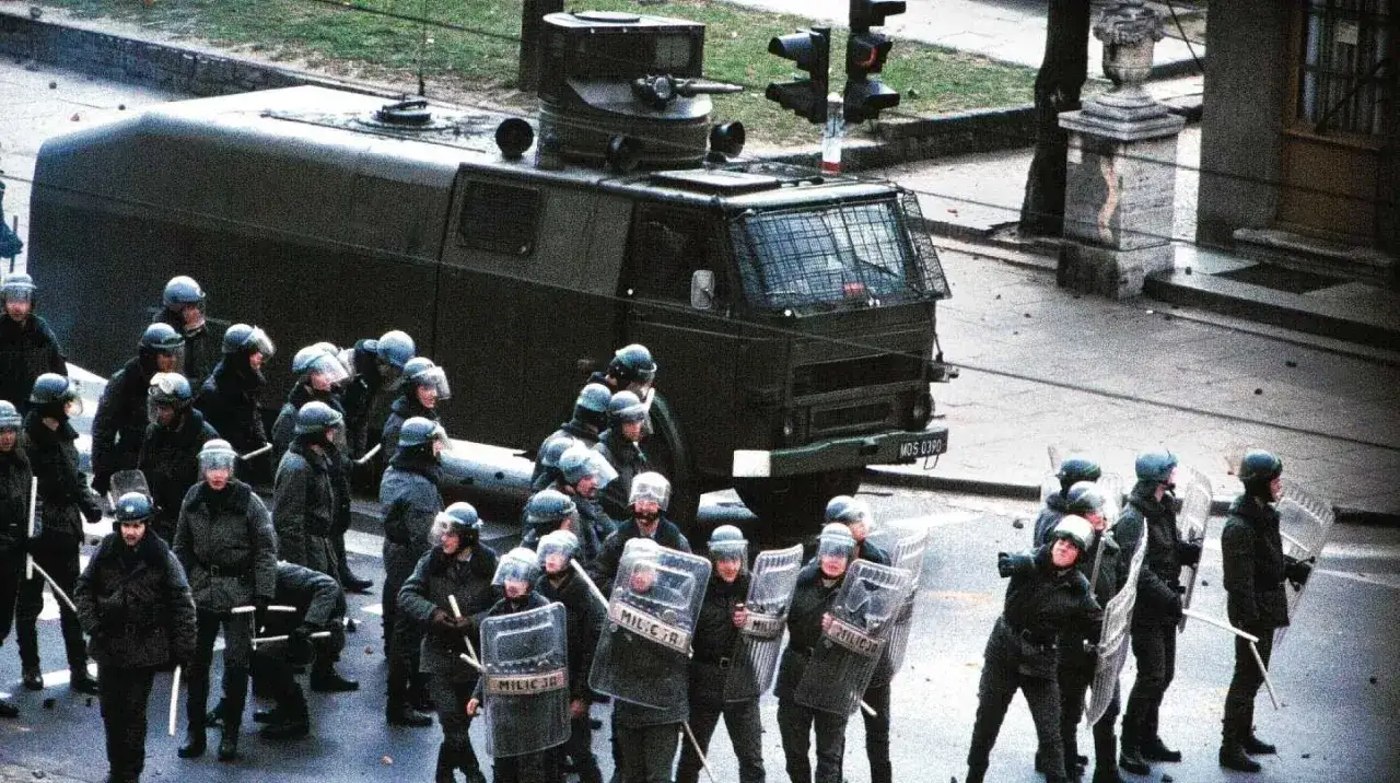 ZOMO w pełnym rynsztunku, z tarczami i pałkami, stoi obok pojazdu opancerzonego.