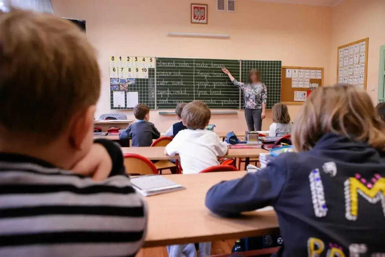 Konfederacja i bon oświatowy: jak system edukacji mógłby działać? Dzieci w klasie słuchają nauczycielki przy tablicy.