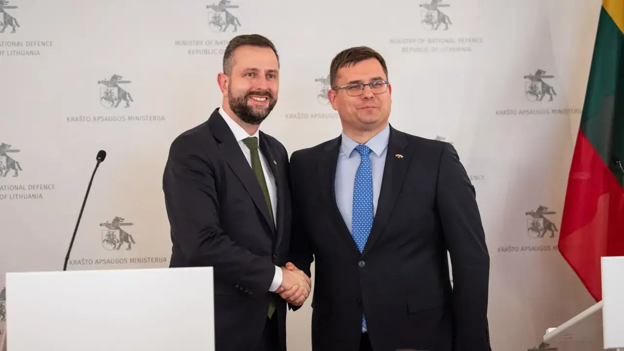 Dwóch mężczyzn w garniturach ściska sobie dłonie. Tło wskazuje na spotkanie dotyczące obronności, być może związane z Polską i Litwą.