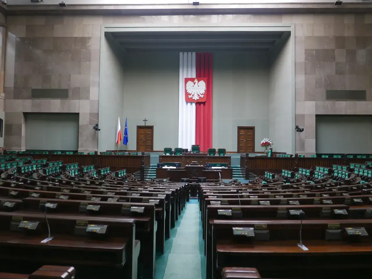 Pusta sala sejmowa, gdzie Koalicja Obywatelska ma rozliczać afery PiS. Widoczne rzędy zielonych foteli i mównice.