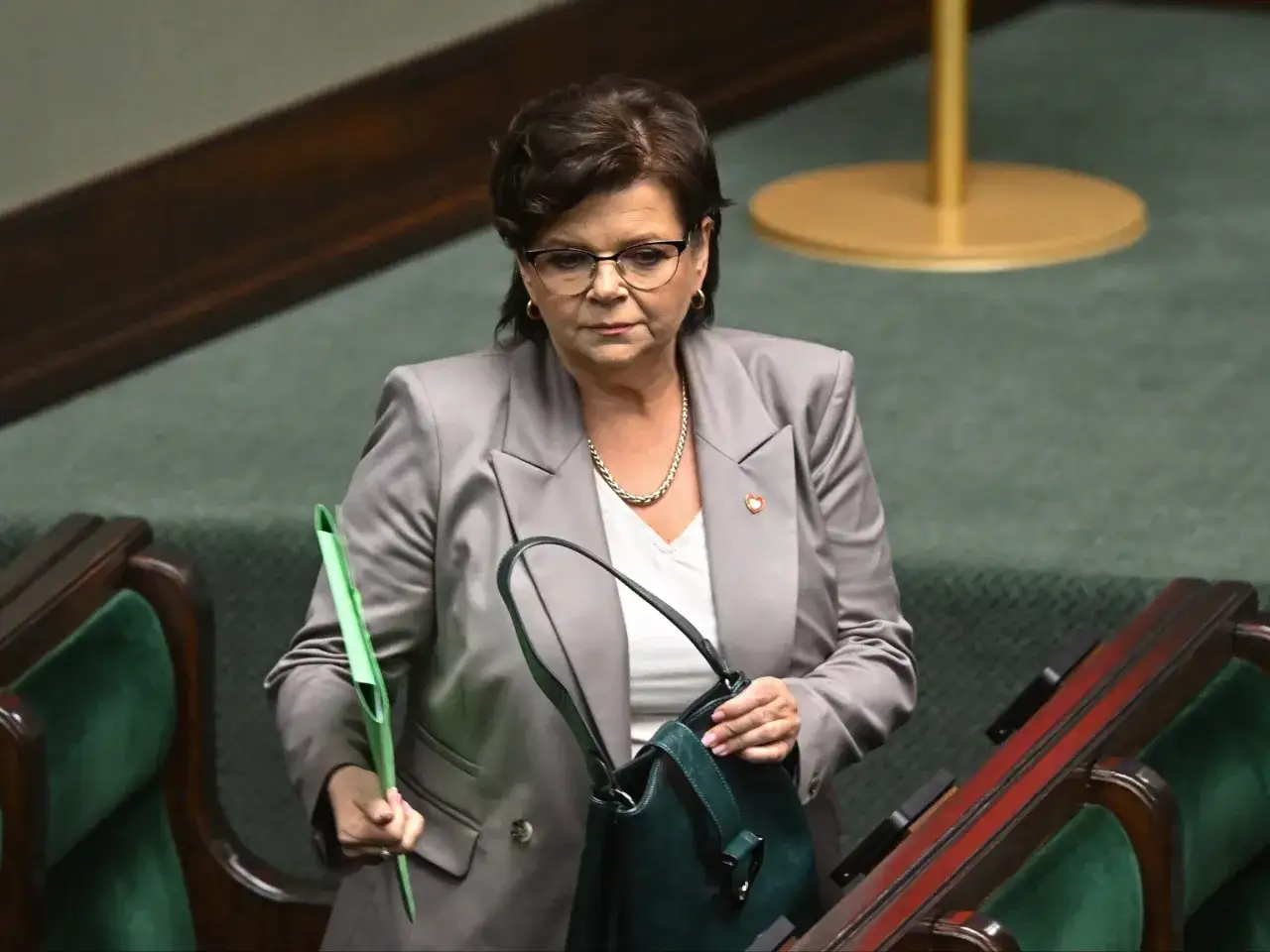 Analiza przetasowań w rządzie Koalicji Obywatelskiej. Polityczka w szarym żakiecie z zieloną teczką i torebką.
