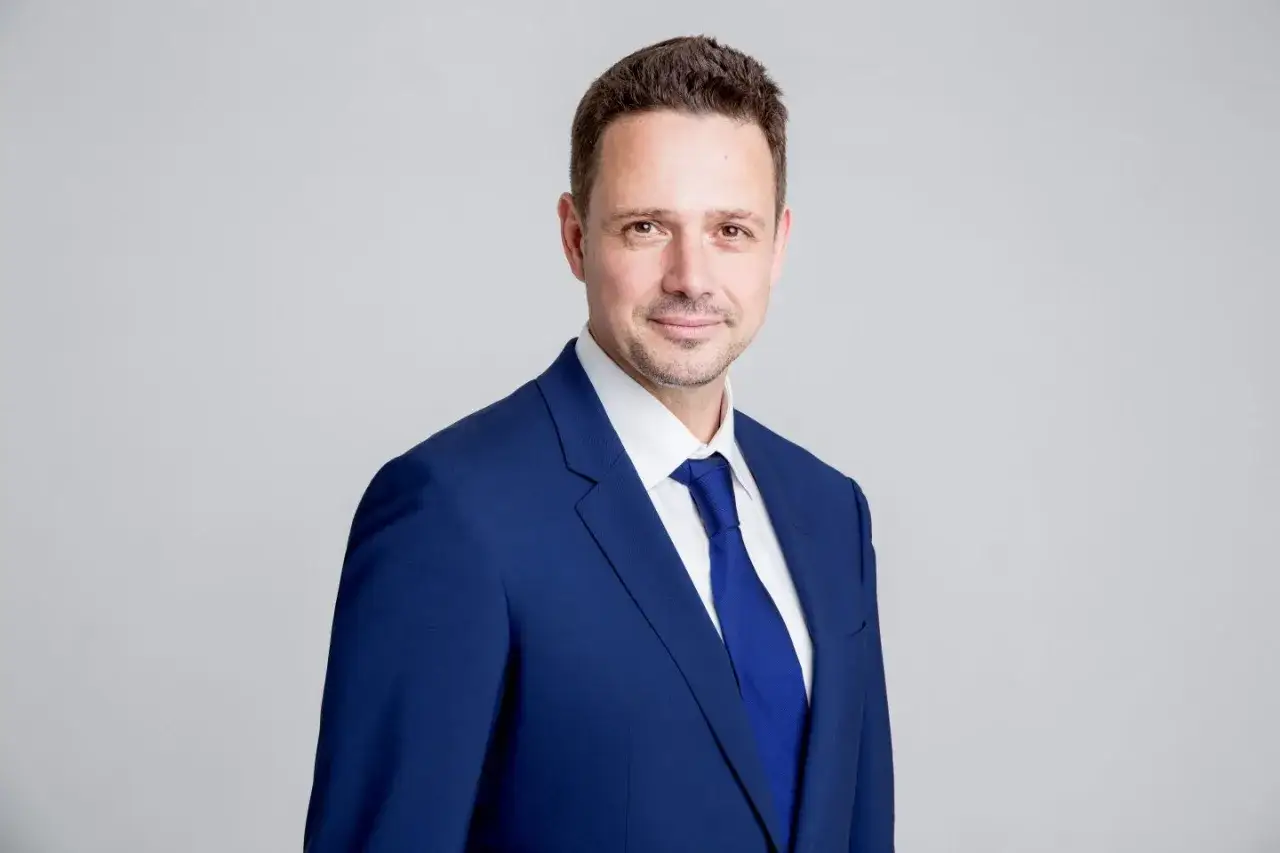 Rafał Trzaskowski w granatowym garniturze i krawacie, uśmiecha się. Mówi płynnie w wielu językach.