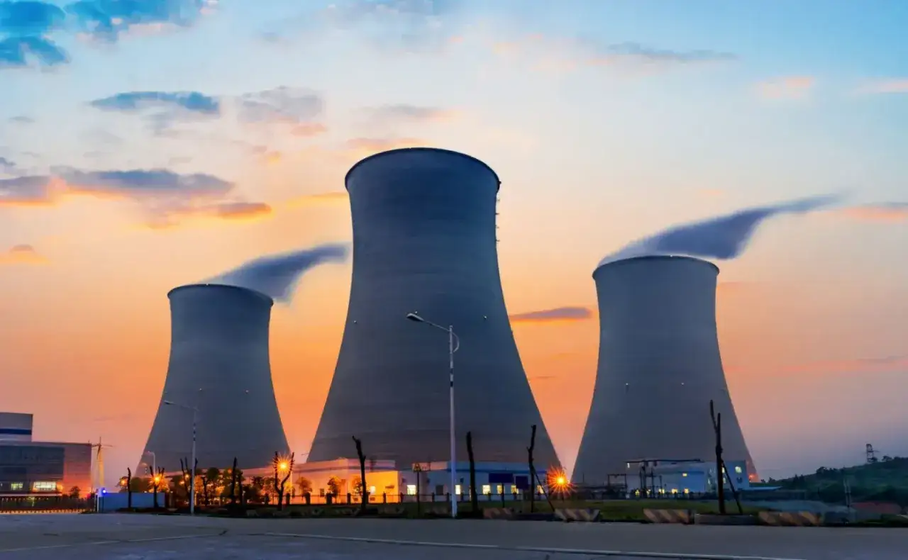 Trzy chłodnie kominowe elektrowni, symbol transformacji energetycznej. Dyskusja o węglu i elektrowniach jądrowych trwa.