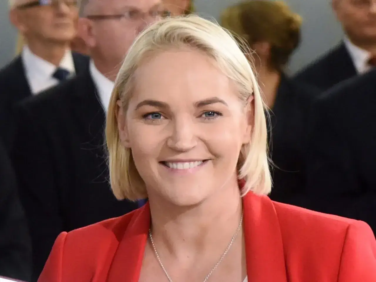 Dominika Chorosińska z uśmiechem, w czerwonej marynarce, w otoczeniu ludzi. Marzy o szczęśliwych dzieciach.