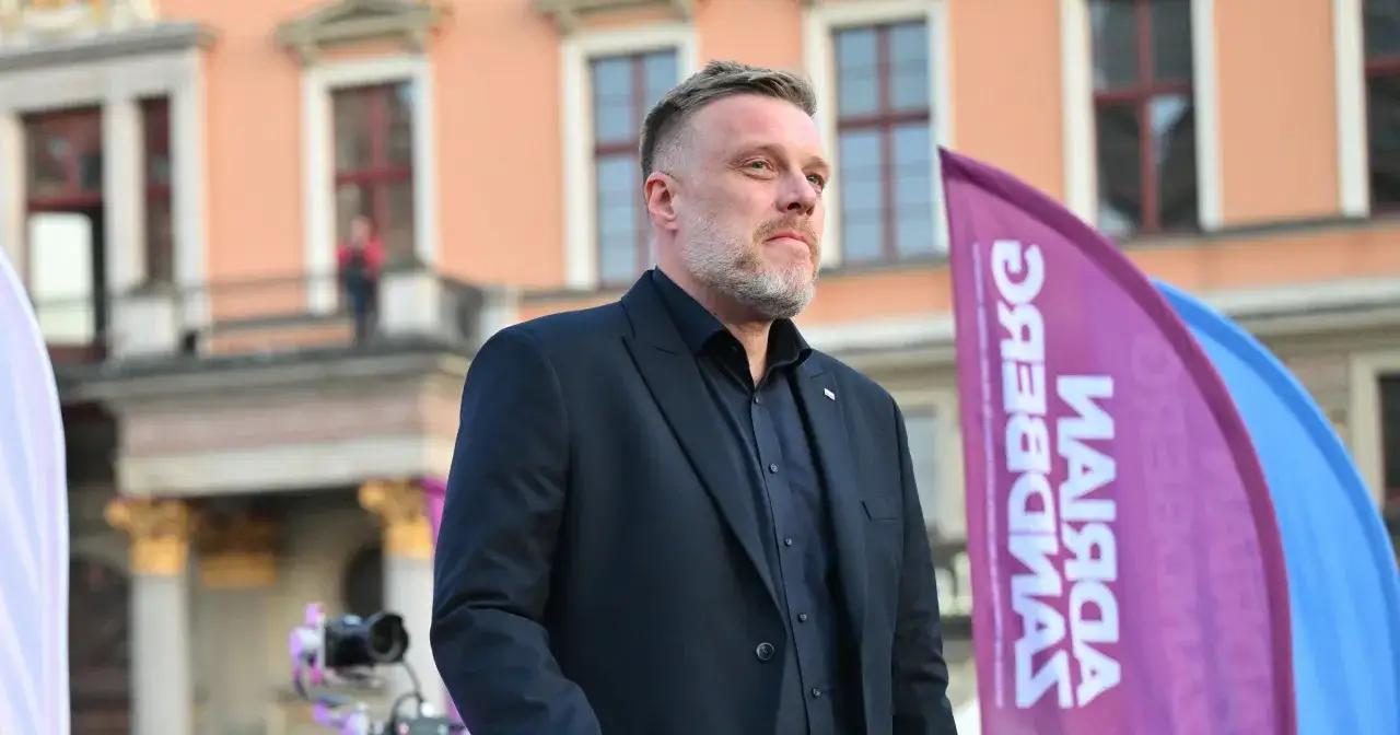 Adrian Zandberg, lider partii Razem, na tle budynku. Flaga z napisem 