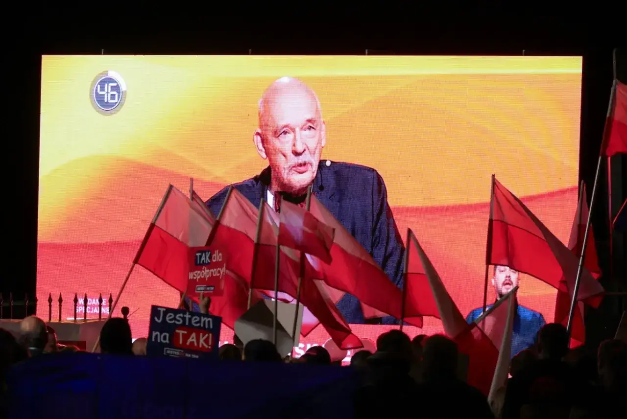 Janusz Korwin Mikke przemawia na tle ekranu z hasłem 