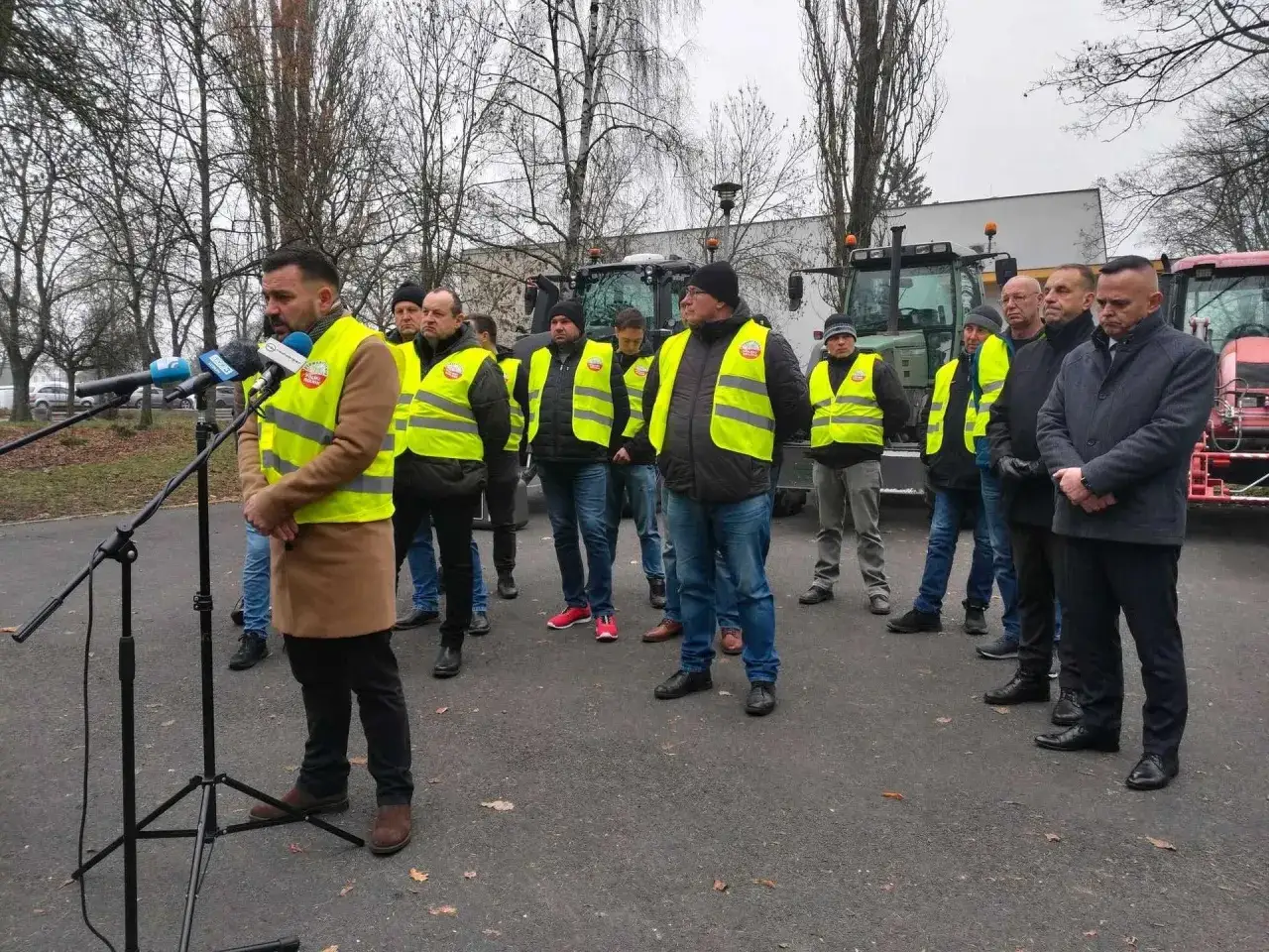 Mężczyzna w kamizelce odblaskowej przemawia do mikrofonów. Grupa rolników w kamizelkach stoi za nim. Lewica a rolnictwo jak odpowiada na postulaty z protestów rolników.