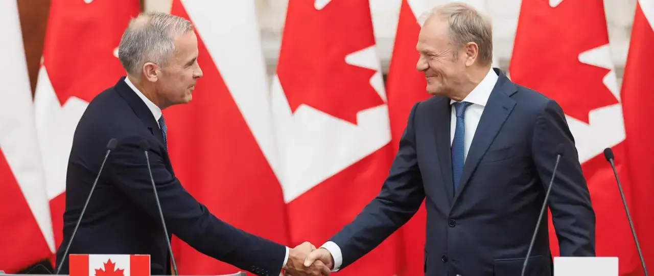 Dwóch polityków ściska sobie dłonie na tle flag Kanady. Wzmocnienie relacji polska-kanada.