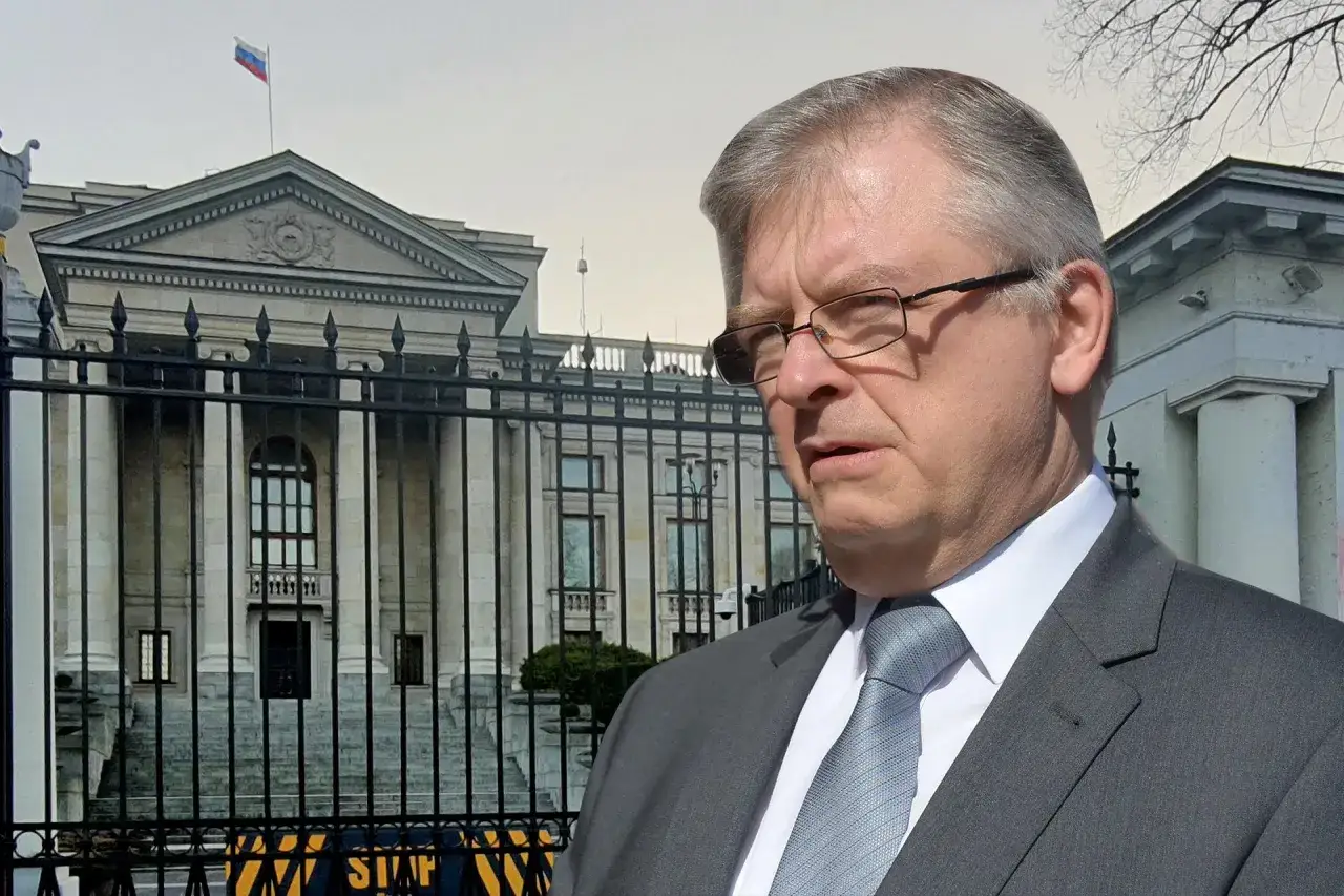 Ambasador Rosji w garniturze przed budynkiem z rosyjską flagą.