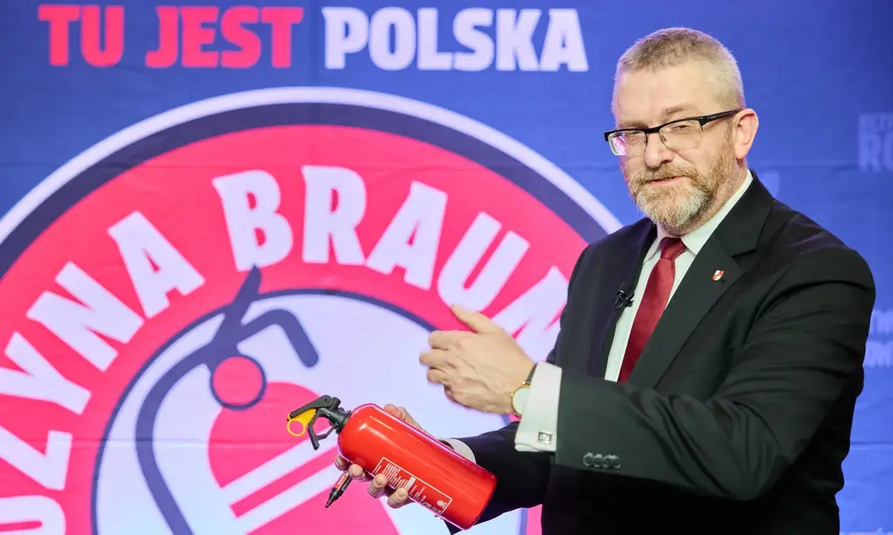 Grzegorz Braun w Sejmie, skandale i realne poparcie dla partii. Polityk trzyma gaśnicę na tle baneru 