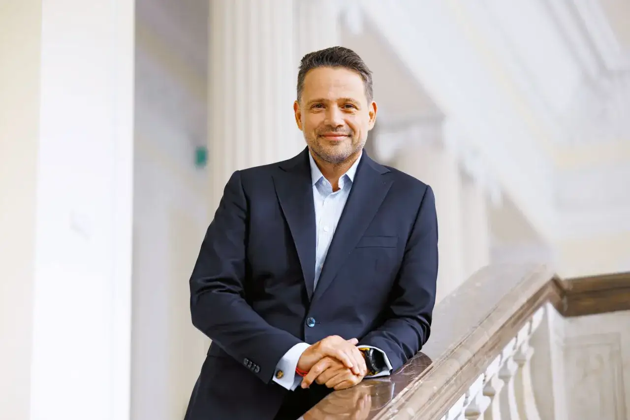 Rafał Trzaskowski, w eleganckim garniturze, opiera się o balustradę. Jego pewna postawa sugeruje, jak Rafał Trzaskowski buduje pozycję wewnątrz Koalicji Obywatelskiej.