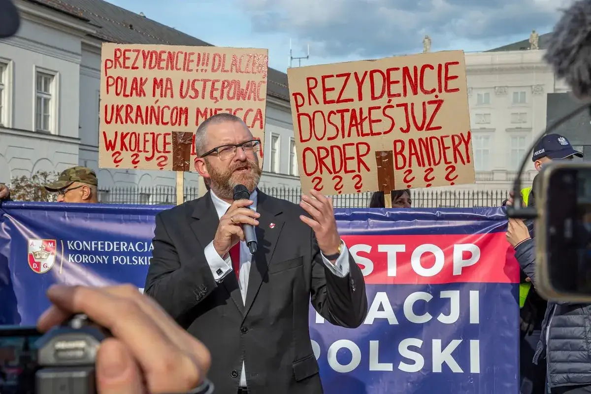 Mężczyzna przemawia na wiecu Konfederacji. Transparenty głoszą 