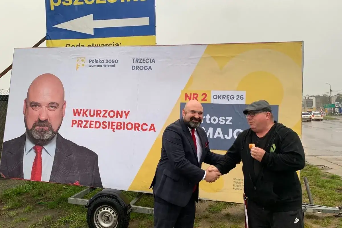 Polska 2050 Szymona Hołowni prezentuje postulaty dla małych i średnich przedsiębiorców. Politycy ściskają dłonie przed banerem.