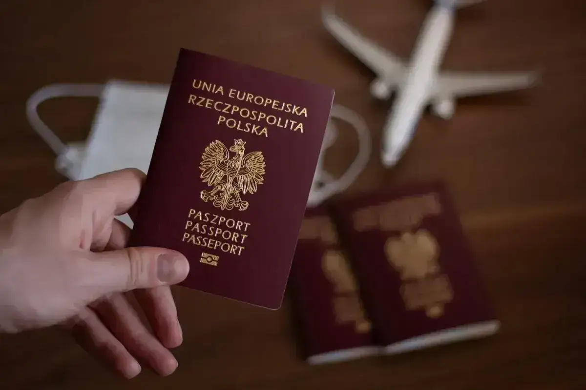Dłoń trzyma polski paszport. Obok leżą kolejne dokumenty, maseczka i samolot. Zastanawiasz się, ile się czeka na paszport?