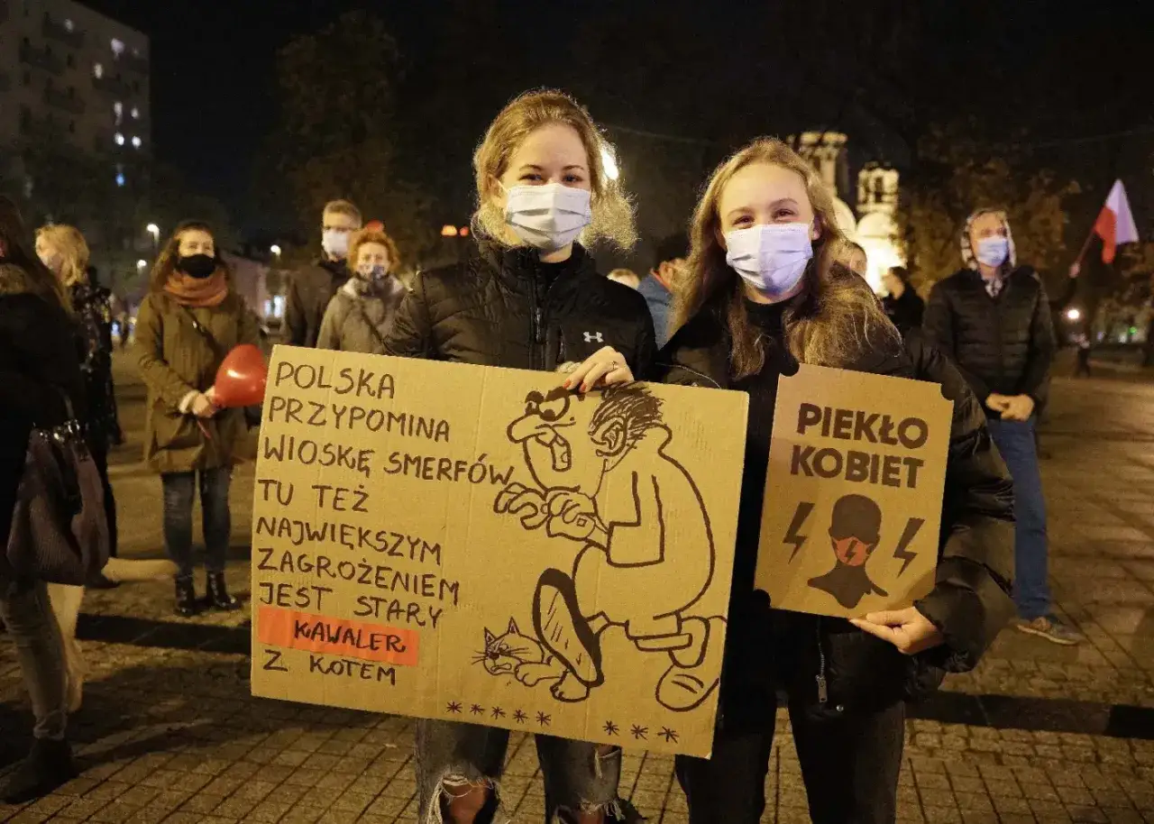 Młode kobiety na proteście trzymają transparenty. Jeden z nich pyta, dlaczego Konfederacja traci poparcie wśród młodych kobiet, porównując Polskę do Wioski Smerfów.