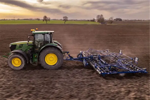Zielony traktor z agregatem uprawowym na polu. Europejski zielony ład: dlaczego lewica popiera unijną politykę klimatyczną.