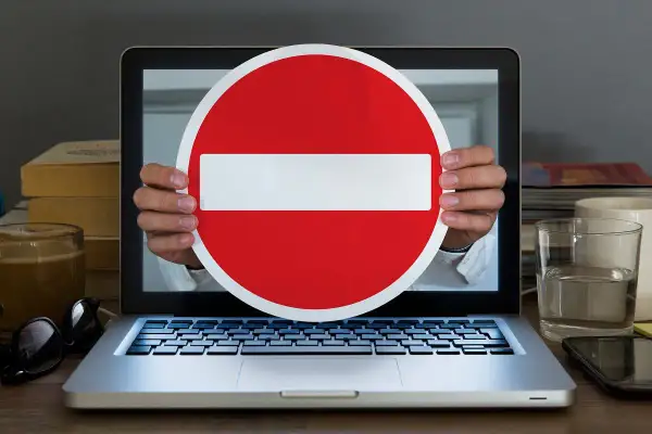 Ręce trzymają znak zakazu przed ekranem laptopa. Symbolizuje to debatę o konfederacji a wolności słowa, projekt ustawy o ochronie w internecie.