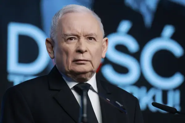 Jarosław Kaczyński w garniturze, na tle niebieskiego napisu.