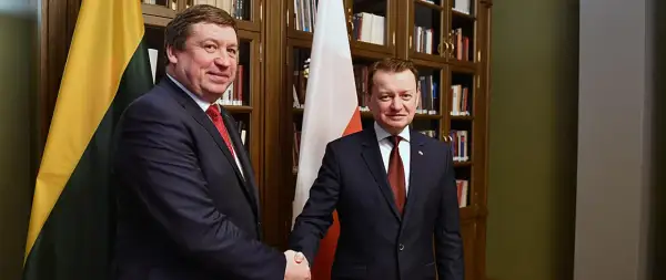 Dwóch polityków ściska sobie dłonie na tle flag Polski i Litwy.