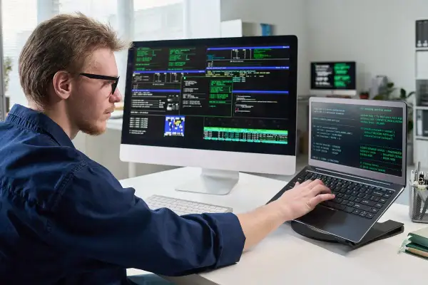 Programista pracuje przy wielu monitorach. Dowiedz się, co Konfederacja proponuje dla branży IT i programistów B2B.