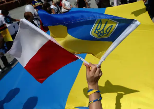 Dłoń trzyma polską i ukraińską flagę. W tle widać ludzi i wielką ukraińską flagę. To symboliczne przedstawienie wpływu koalicji obywatelskiej na relacje Polski z Ukrainą.