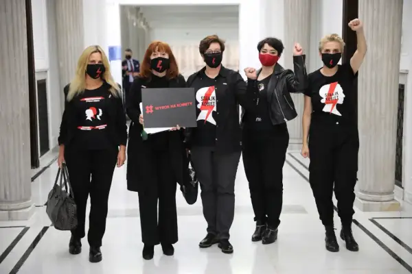 Kobiety w czarnych koszulkach "Strajk Kobiet" i maskach, z hasłem "Wyrok na kobiety", symbolizują siłę lewicy i jej zaangażowanie w protesty.