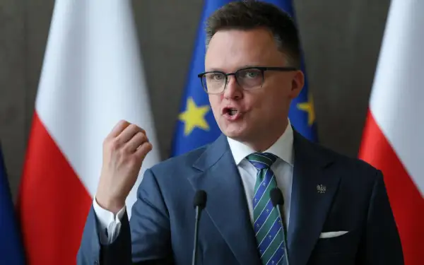Szymon Hołownia, w garniturze i z flagami Polski i UE, przemawia. Czy jest konserwatystą? Ewolucja poglądów politycznych.