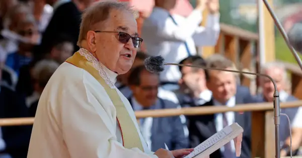 Ojciec Tadeusz Rydzyk przemawia do mikrofonu. W tle widać ludzi, a także fragmenty budowli. W czasach rządu PiS, fundacje związane z ojcem Rydzykiem otrzymywały znaczące dotacje.