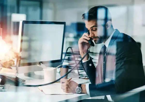 Biznesmen w garniturze rozmawia przez telefon, notując. Czasem nawet siła wyższa nie przeszkodzi w pracy.