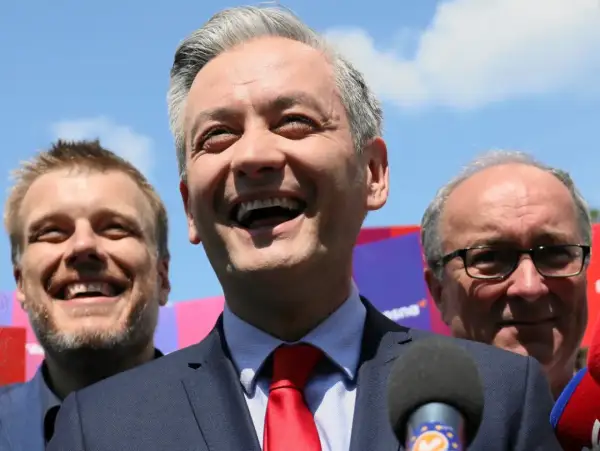 Uśmiechnięty polityk z czerwonym krawatem, w otoczeniu innych mężczyzn. Analiza struktury elektoratu partii, kogo reprezentuje lewica.