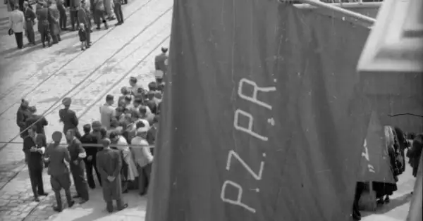 Tłum ludzi zgromadzony na ulicy, na pierwszym planie widoczna wielka, ciemna tkanina z napisem PZPR.