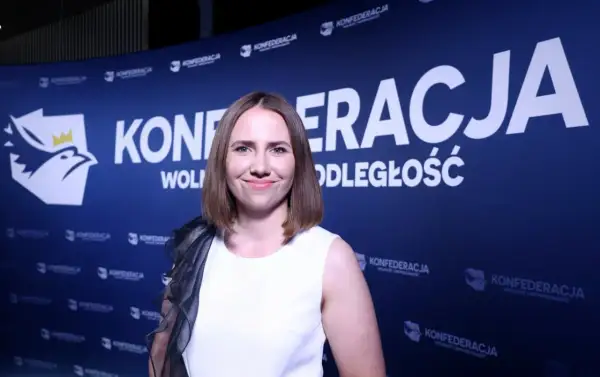 Uśmiechnięta kobieta na tle niebieskiego banera z logo i napisem "KONFEDERACJA WOLNOŚĆ I NIEPODLEGŁOŚĆ".