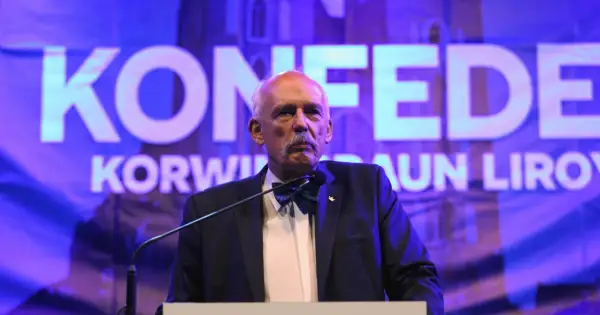 Janusz Korwin-Mikke, znany z kontrowersyjnych poglądów, przemawia na tle napisu "Konfederacja".