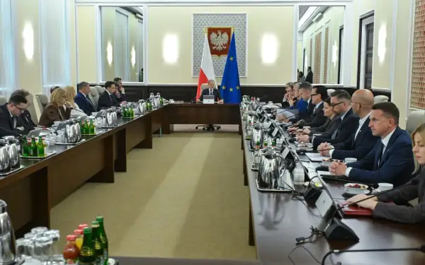 Uczestnicy spotkania przy długim stole, dyskutują o budżetowym deficycie. Na stole napoje i dokumenty.